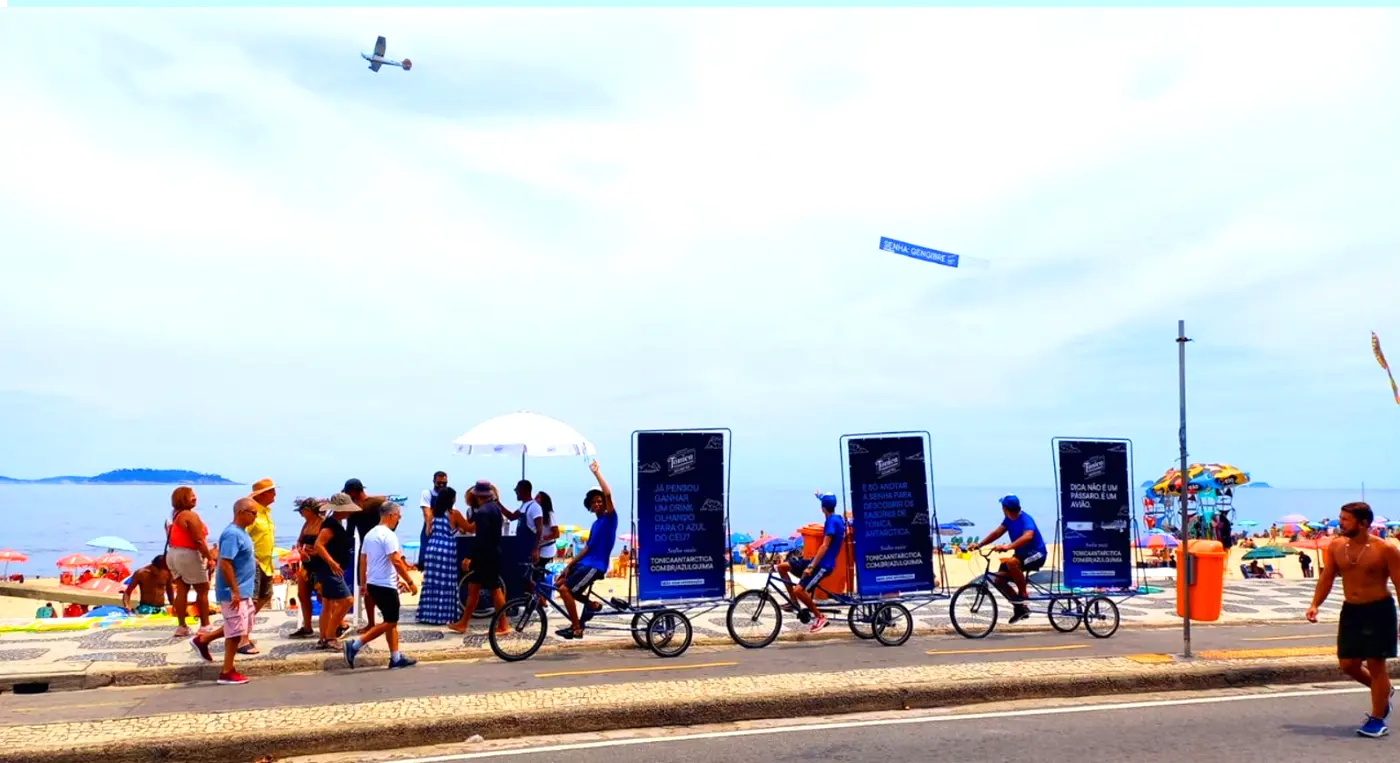 Avião com faixa aérea da Tônica Antarctica sobre Ipanema enquanto bikedoors circulam no calçadão