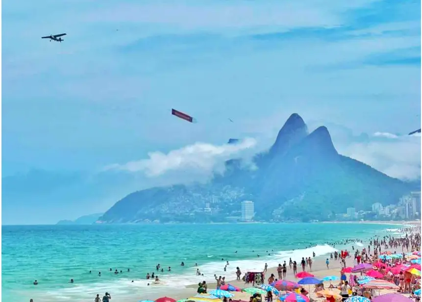 Faixa aérea sobrevoando a praia de Ipanema lotada no verão